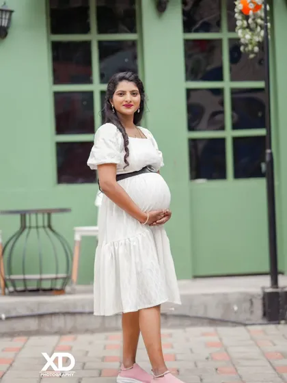 A chic solo portrait of the mother-to-be in a simple white dress against a modern green backdrop.