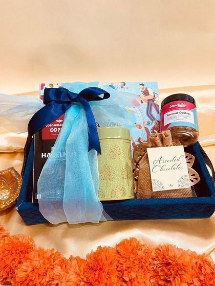A deep blue tray hamper filled with coffee, assorted chocolates, and almond cookies. The blue tulle wrapping adds a touch of sophistication to this Diwali gift.