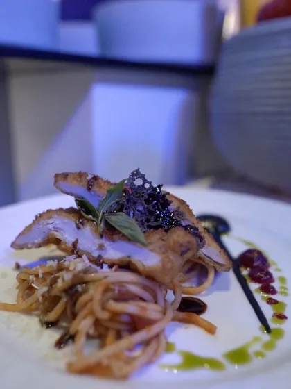 A sophisticated main course of sliced chicken breast served over spaghetti with a rich sauce, demonstrating our fusion of Italian techniques with global flavours.