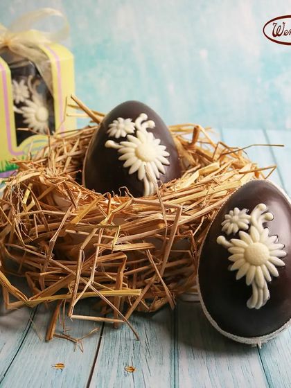 Our chocolate Easter eggs nestled in a straw nest. Each egg is decorated with a delicate white chocolate flower, showcasing our bakers' craftsmanship.