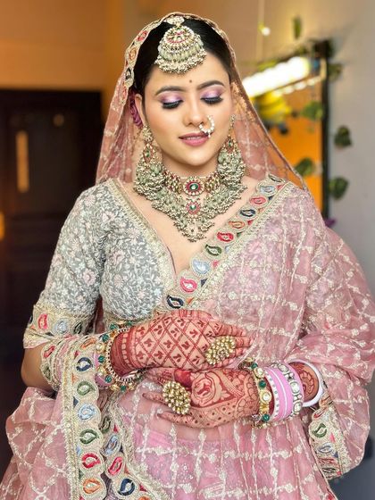 The full look of the pastel pink lehenga, showing the detailed embroidery and the bride's henna-adorned hands.