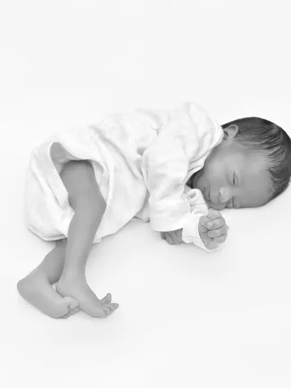 A full-body shot of a sleeping newborn in black and white. This minimalist composition emphasizes the baby's tiny, curled form and the peacefulness of their sleep.