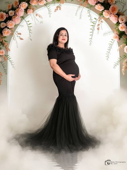 A dramatic solo portrait in a black mermaid-style gown. The floral arch and smoke effect add a touch of glamour and mystery.