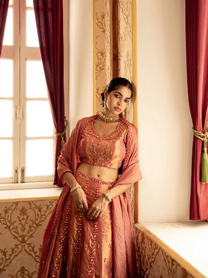 A relaxed, elegant pose by a window, capturing the soft drape of the lehenga and the warmth of the natural light. This image was created for a brand's lookbook to show the garment's wearability.