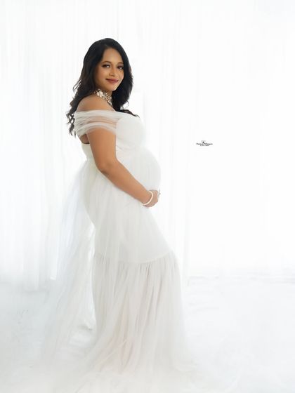 A classic high-key portrait against a bright white background. The mother-to-be looks radiant and ethereal in her simple white gown.