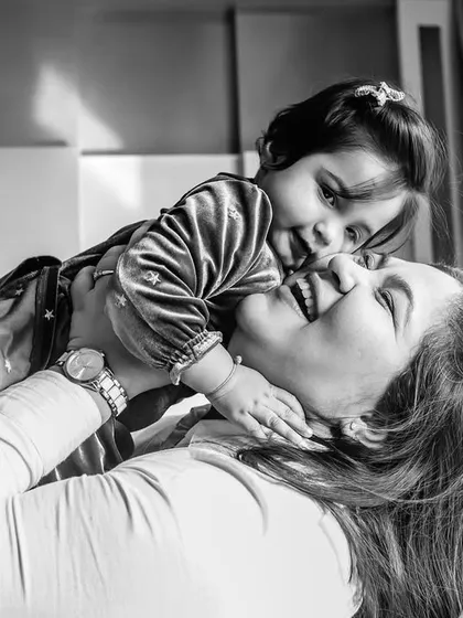 A playful black and white photo of a mother lifting her child in the air. The image is filled with joy and captures the special bond they share.
