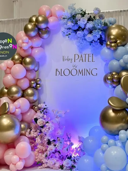 A stunning "Baby is Blooming" gender reveal backdrop. The design uses a split color scheme of pink and blue balloons, accented with chrome gold and florals, creating a dramatic and exciting setting for the big reveal.