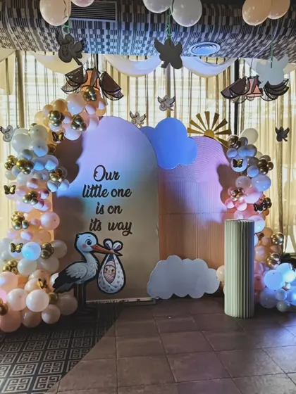 A charming storybook theme with the message "Our little one is on its way". The decoration features a stork carrying a baby, butterfly cutouts, and cloud props for a whimsical and sweet baby shower.