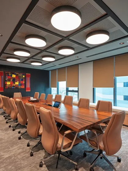 An executive boardroom with a live-edge wood table and comfortable leather chairs. The coffered ceiling with circular light fixtures provides excellent acoustics and a sophisticated aesthetic.