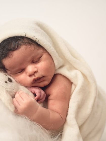 Swaddled in a soft white hooded blanket, this newborn sleeps peacefully. This minimalist approach creates a pure and angelic portrait.