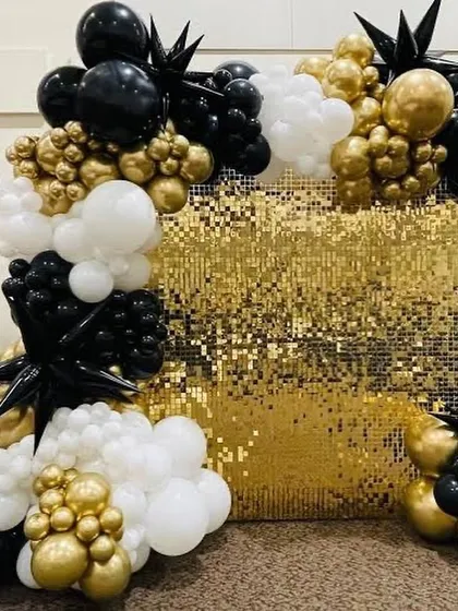 A close-up of a gold sequin wall framed by a balloon arrangement in black, white, and gold. The mix of textures and colors creates a very luxurious and festive feel.