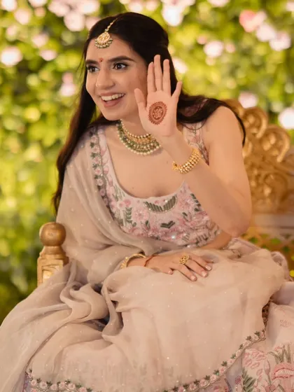 The bride showing her mehndi. The soft floral background and her happy expression make for a beautiful, classic portrait.