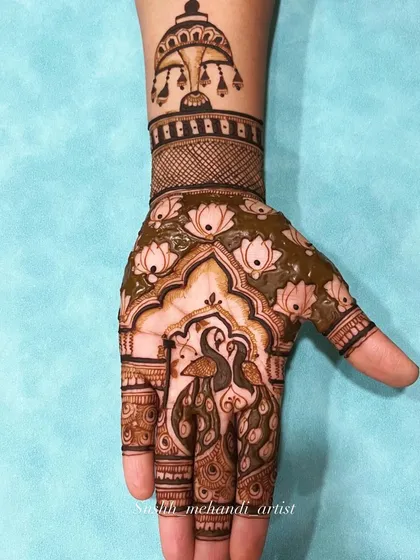 A graceful design featuring two peacocks on the palm, surrounded by lotus flowers and a decorative umbrella motif on the wrist.