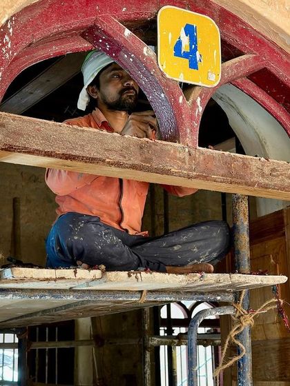 A worker perched in an arched window transom, carefully restoring the wooden frame. These high, hard-to-reach places require special care and attention to detail.