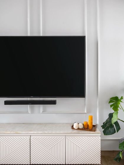A close-up of a Scandinavian-inspired living room. The TV console features a CNC-milled geometric pattern on the shutters, topped with a marble-finish laminate for a touch of timeless elegance.