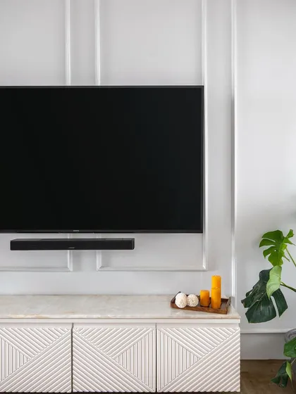 A close-up of a Scandinavian-inspired living room. The TV console features a CNC-milled geometric pattern on the shutters, topped with a marble-finish laminate for a touch of timeless elegance.