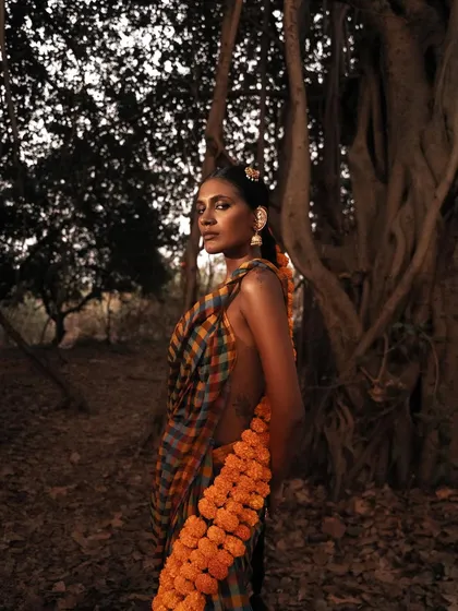 A profile shot that captures the model within the dense forest, with the marigold garland adding a pop of color. The lighting feels natural and atmospheric.