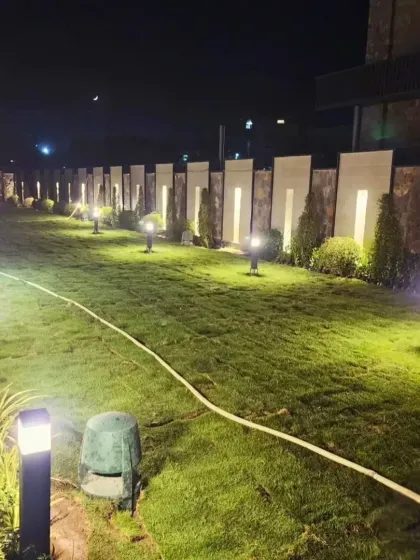 A wide shot of the completed lawn at night, showing the full expanse of the green space. The landscape lighting enhances the beauty of the fresh turf.