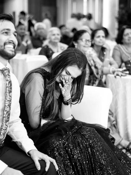 A candid black and white photo of the bride laughing heartily during the speeches at her cocktail party.