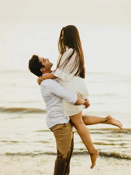 A joyful and playful moment on the beach, as the groom lifts his bride into the air. Their laughter and the beautiful seaside setting create a feeling of carefree love and happiness.