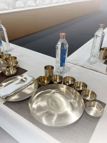 An elegant table setting with traditional bronze 'kansa' thalis. This heritage tableware adds a touch of timeless class to the dining experience.