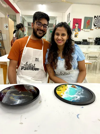 A couple proudly holds up their resin art pieces, one a galaxy design and the other a beautiful beach scene.