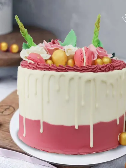 A gorgeous macaron-topped drip cake in shades of pink and white, with a touch of gold. This elegant and delicious cake is perfect for a stylish celebration.