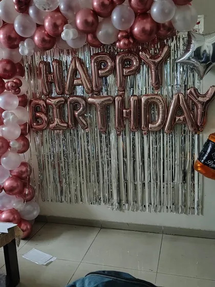 A birthday photo corner at home with a rose gold and white balloon frame against a silver fringe curtain.