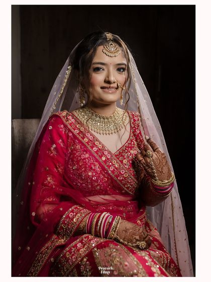 A classic bridal portrait, capturing the bride's gentle smile and the intricate details of her red lehenga and jewelry.