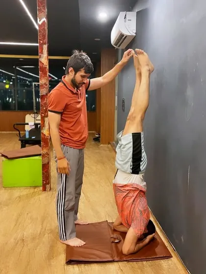 Assisting a student with a wall-supported headstand, ensuring his shoulders are engaged and his neck is safe.