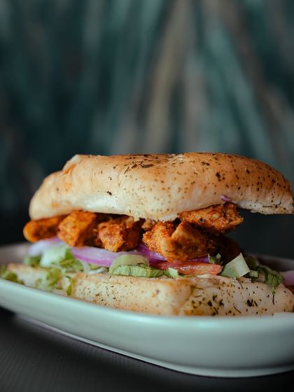 A side profile of the Chicken Tikka Panini, showcasing the generous filling of chicken and vegetables, all held together by a perfectly grilled bun.