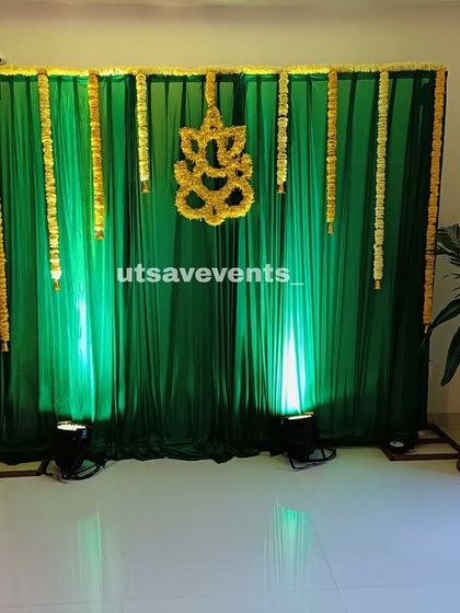 A minimalist traditional backdrop with green drapes and a Ganesha motif made of yellow flowers. This design is ideal for smaller, intimate ceremonies at home.