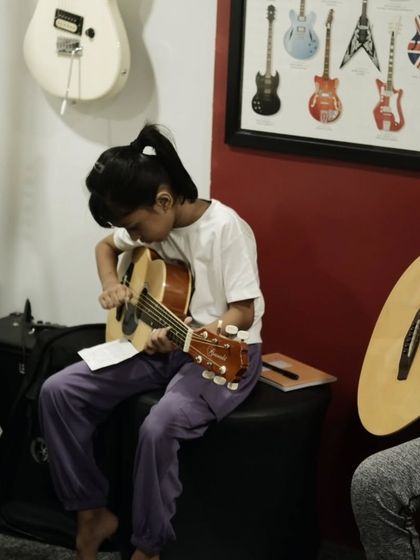 An instructor gives one on one guidance to a young student on her guitar posture and finger placement. These fundamentals are key to progress.