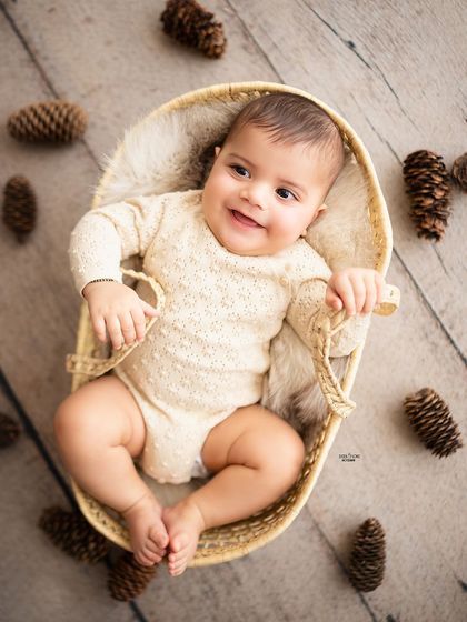 An overhead shot of a happy baby lying in a basket, surrounded by pinecones.