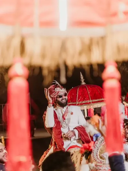 The same energetic baraat moment in color, highlighting the vibrant red of the traditional umbrellas.