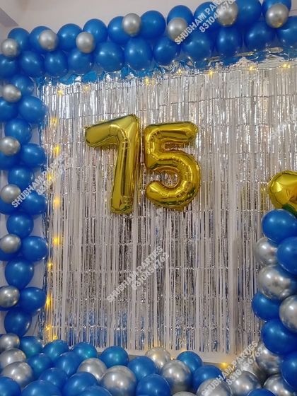 A 75th birthday party decoration with a blue and silver balloon frame and a shimmering backdrop.