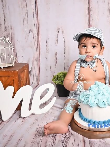 A classic cake smash moment, with frosting on the face and a look of pure satisfaction. This rustic, wood-themed setup is perfect for a little gentleman's first birthday.