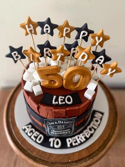A cake for a milestone 50th birthday, designed to look like a Jack Daniel's whiskey barrel. The theme "Aged to Perfection" was perfect! All the details, from the wood grain texture to the sugar "ice cubes" and custom star toppers, were made to create a memorable celebration cake for him.