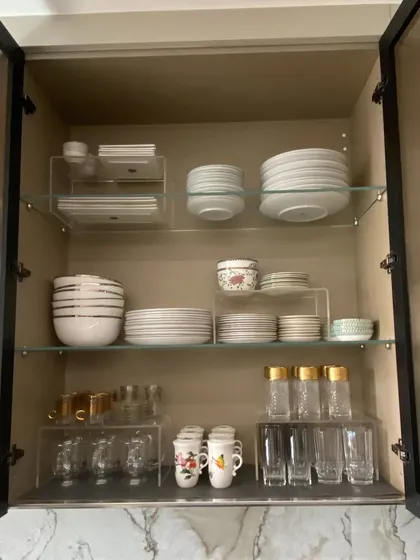 This cabinet uses glass shelves and acrylic risers to create a multi-level display for plates, bowls, and glasses. It maximizes vertical space while keeping everything visible.