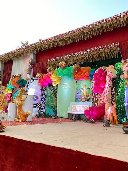The main stage of this outdoor jungle party is filled with life-sized 3D props of elephants, giraffes, and tigers, set against animal-print backdrops and colorful balloon clusters.