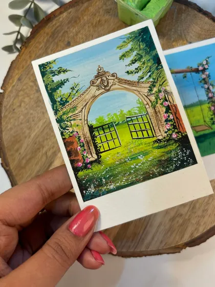 This polaroid features a painting of a vintage gate opening into a lush garden. It’s very cottagecore and dreamy.