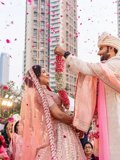 A beautiful shot of the couple mid-varmala, with flower petals raining down on them, creating a magical, celebratory frame.