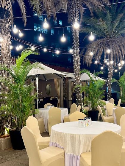 An elegant poolside dining setup. The combination of string lights wrapped around palm trees and classic table settings made for a sophisticated outdoor event.