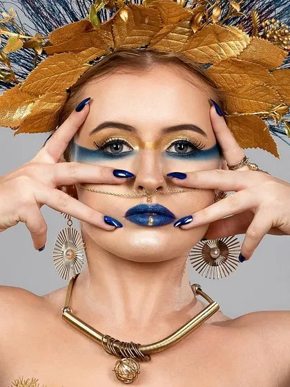 A creative beauty portrait featuring a model with an elaborate golden and blue feathered headpiece and matching bold makeup. This is an example of my work with avant-garde beauty concepts.