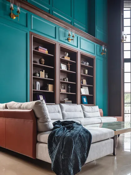A double-height library and living space in the Wanderlust Villa. The bold teal wall, extensive built-in shelving, and grand scale create a dramatic and unforgettable room.