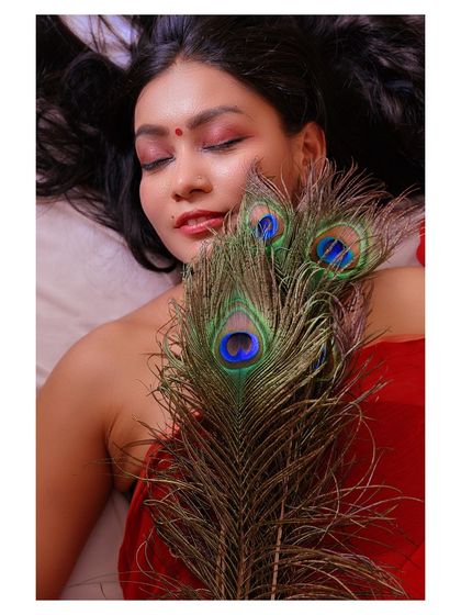 An artistic portrait using a peacock feather as a prop. The model's closed eyes and serene expression create a meditative and beautiful image.
