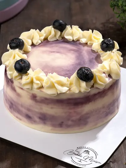A beautiful lemon blueberry cake, showcasing the marbled frosting and fresh blueberry topping. The image is bright and fresh, perfect for a summer dessert.