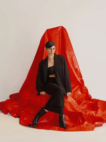 A full-length shot where the red fabric backdrop becomes a sculptural element. The model's all-black outfit stands out powerfully against the color.