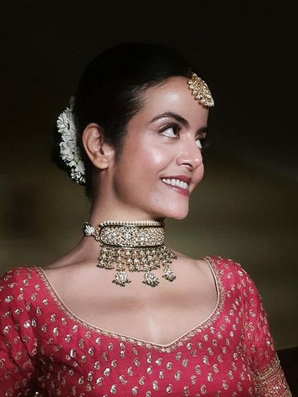 A smiling bride with a classic, clean makeup look and a traditional hair bun adorned with fresh white flowers. This side profile highlights the neatness of the hairstyle and the radiance of her skin.