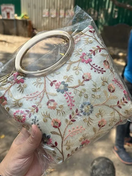 A beautiful white clutch with colourful floral embroidery and a large ring handle. This is a perfect evening bag sourced from a Delhi market.